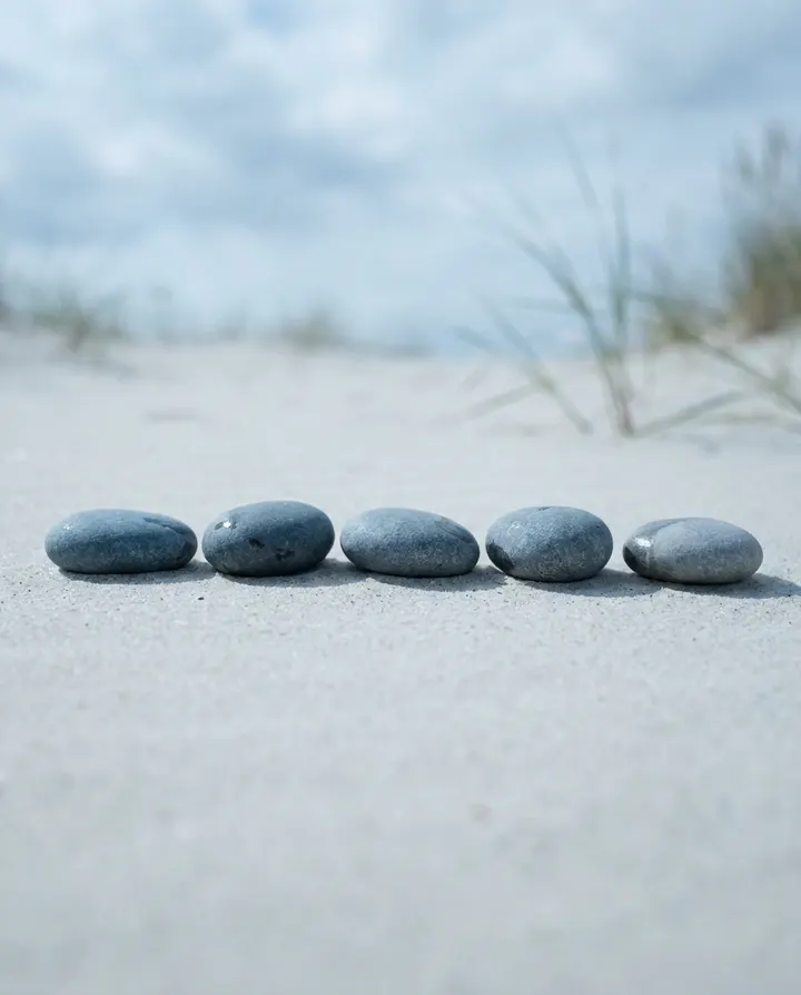 Five grey stones in a row on pale sand, a frame from a top-five list Short