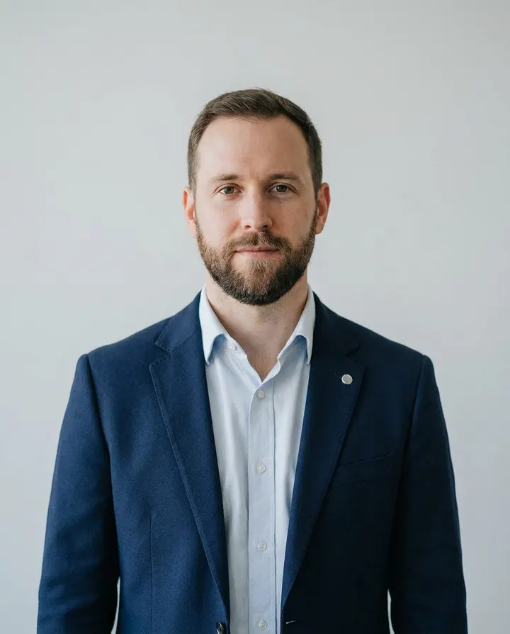 A presenter in a navy blazer against a plain studio backdrop, a frame from a product launch video