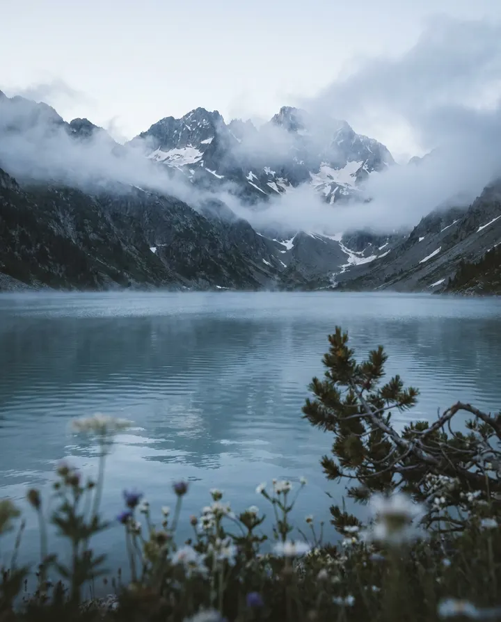 An alpine lake at dawn with clouds over the peaks, a frame from an animated landscape